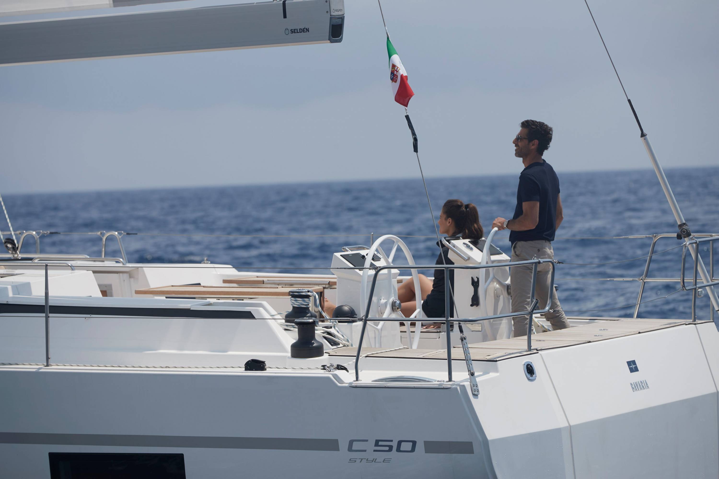 Mann am Steuer einer Segelyacht mit italienischer Flagge.