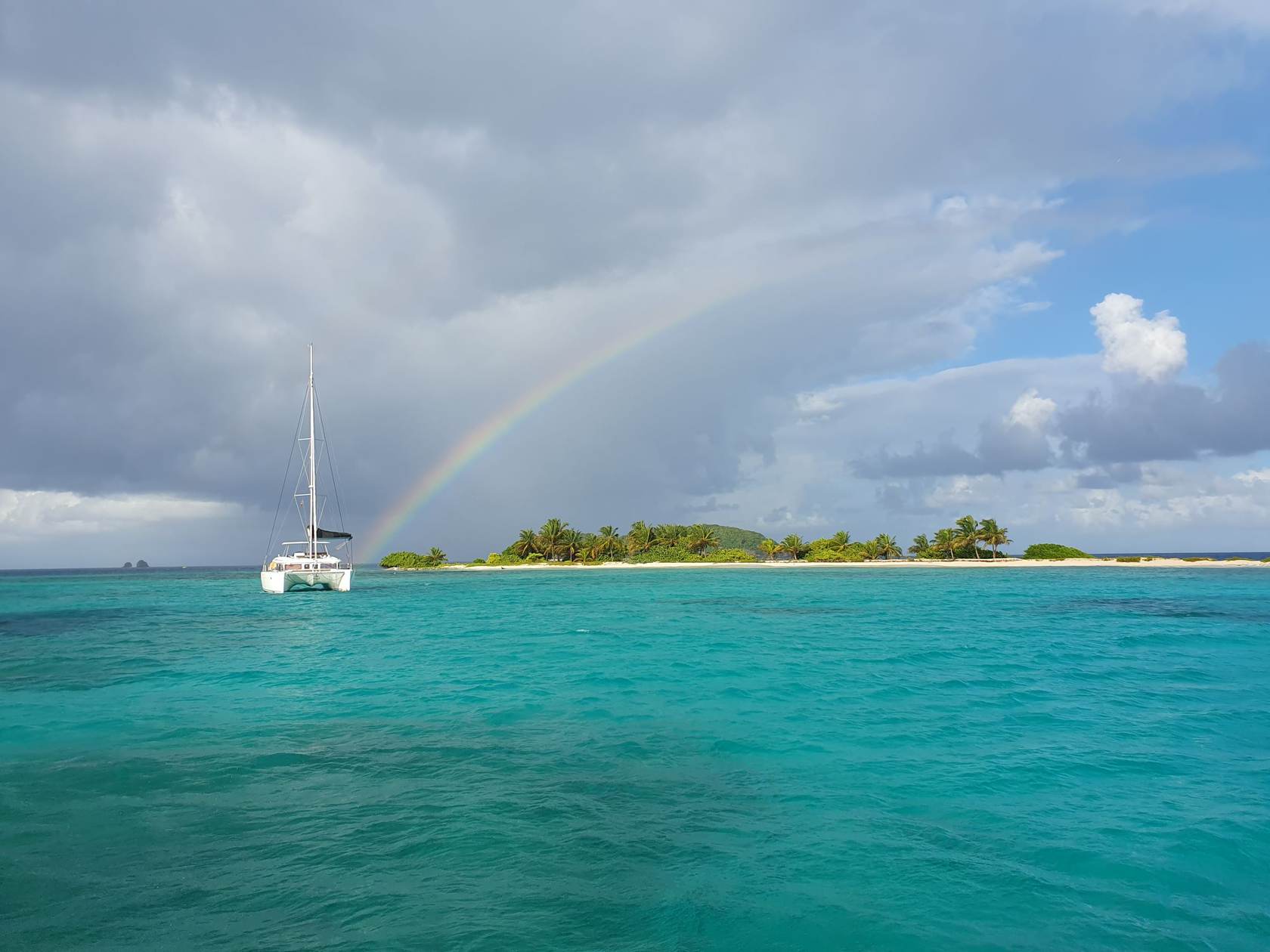 Regenbogen über einer Karibikinsel mit Katamaran vor Anker liegend.