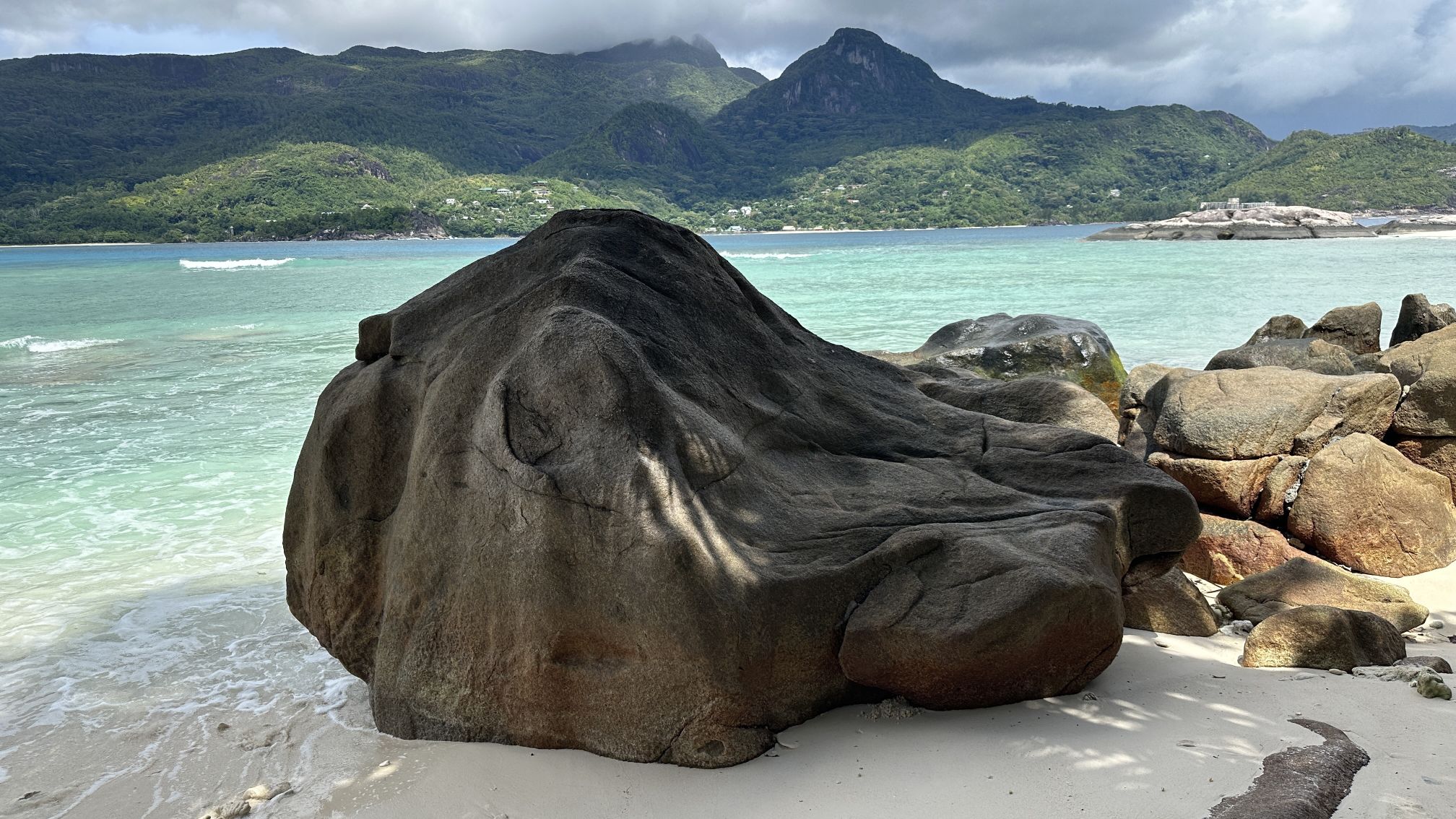 Glatt geschliffener Felsen an einem weißen Sandstrand auf den Seychellen vor blass-grünem Wasser