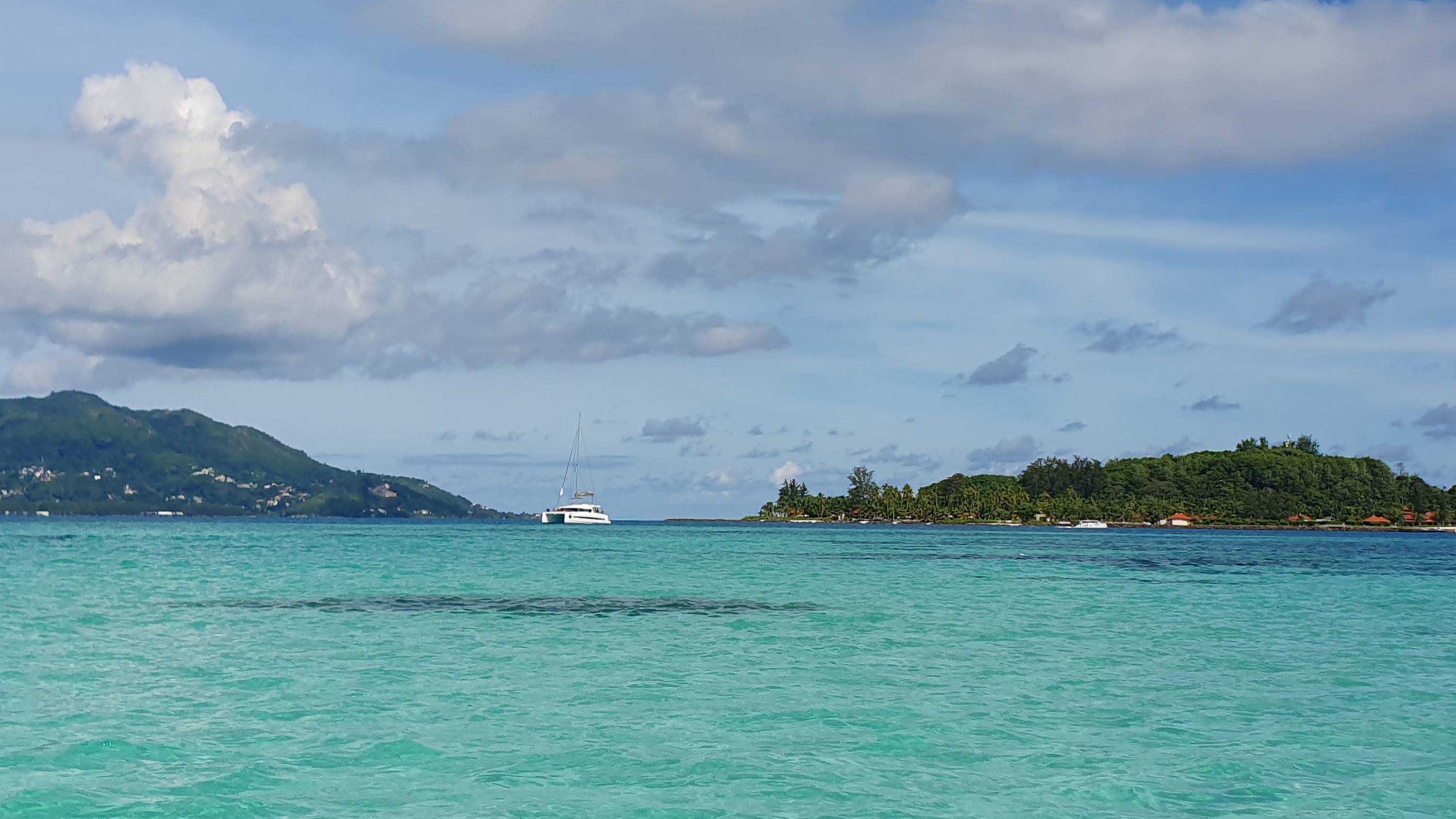 Katamaran vor Anker auf türkisfarbenen Wasser. Im Hintergrund zwei Inseln.