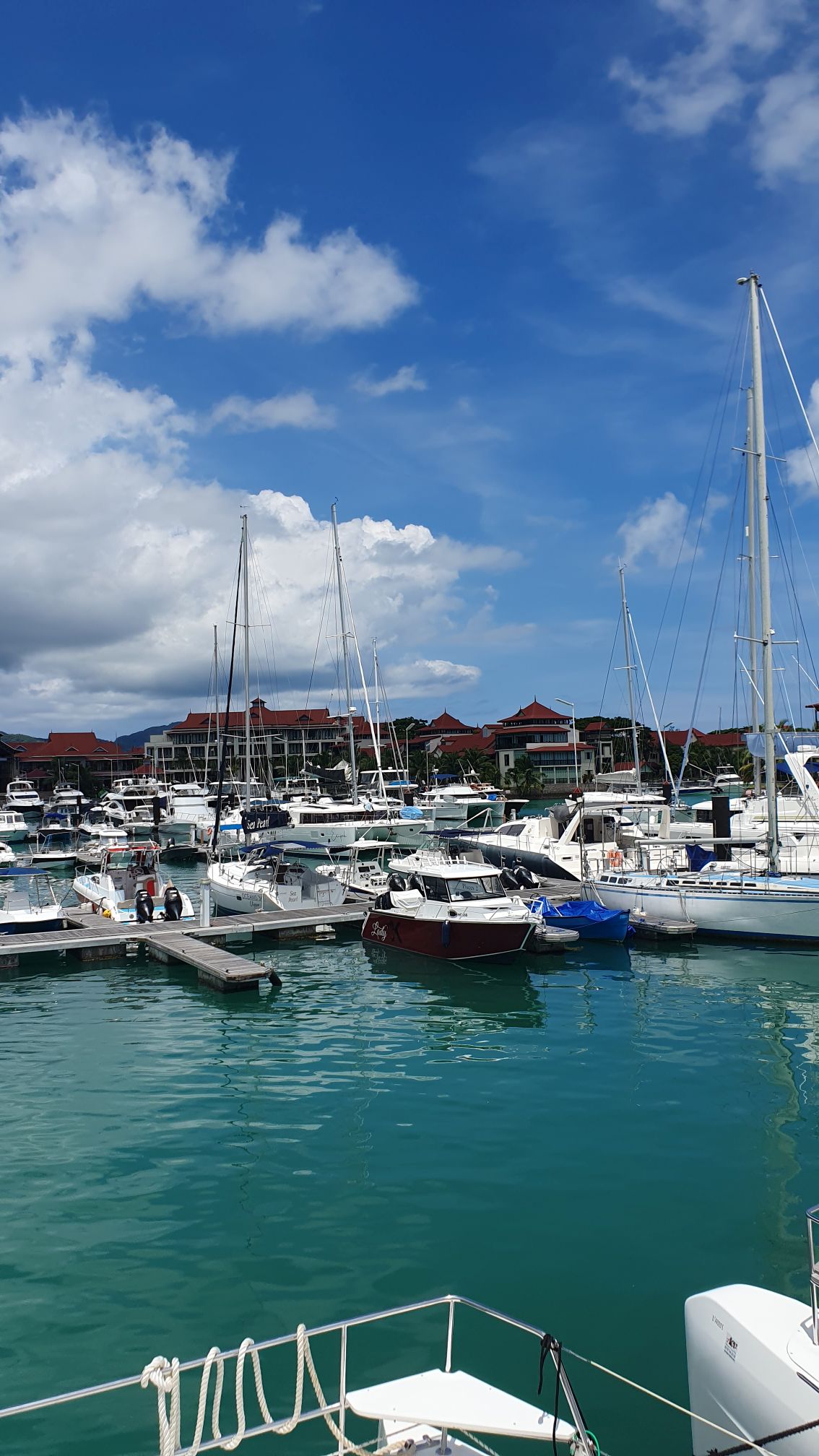Hafenanlage von Mahé mit an Stegen vertäuten Schiffen und den Häusern der Marinaanlage im Hintergrund