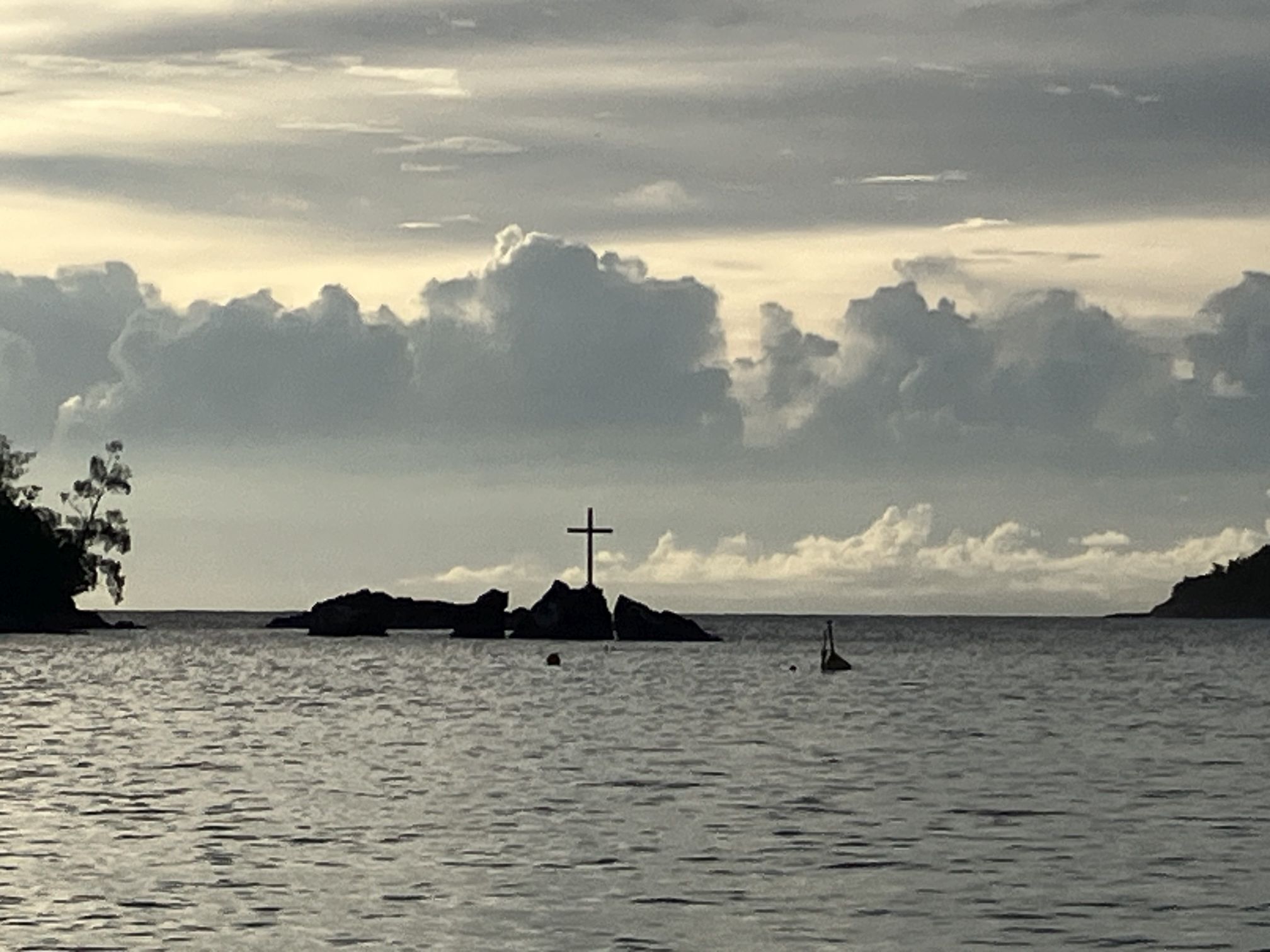 Felsen im Wasser mit einem Kreuz auf der Spitze bei Sonnenuntergang