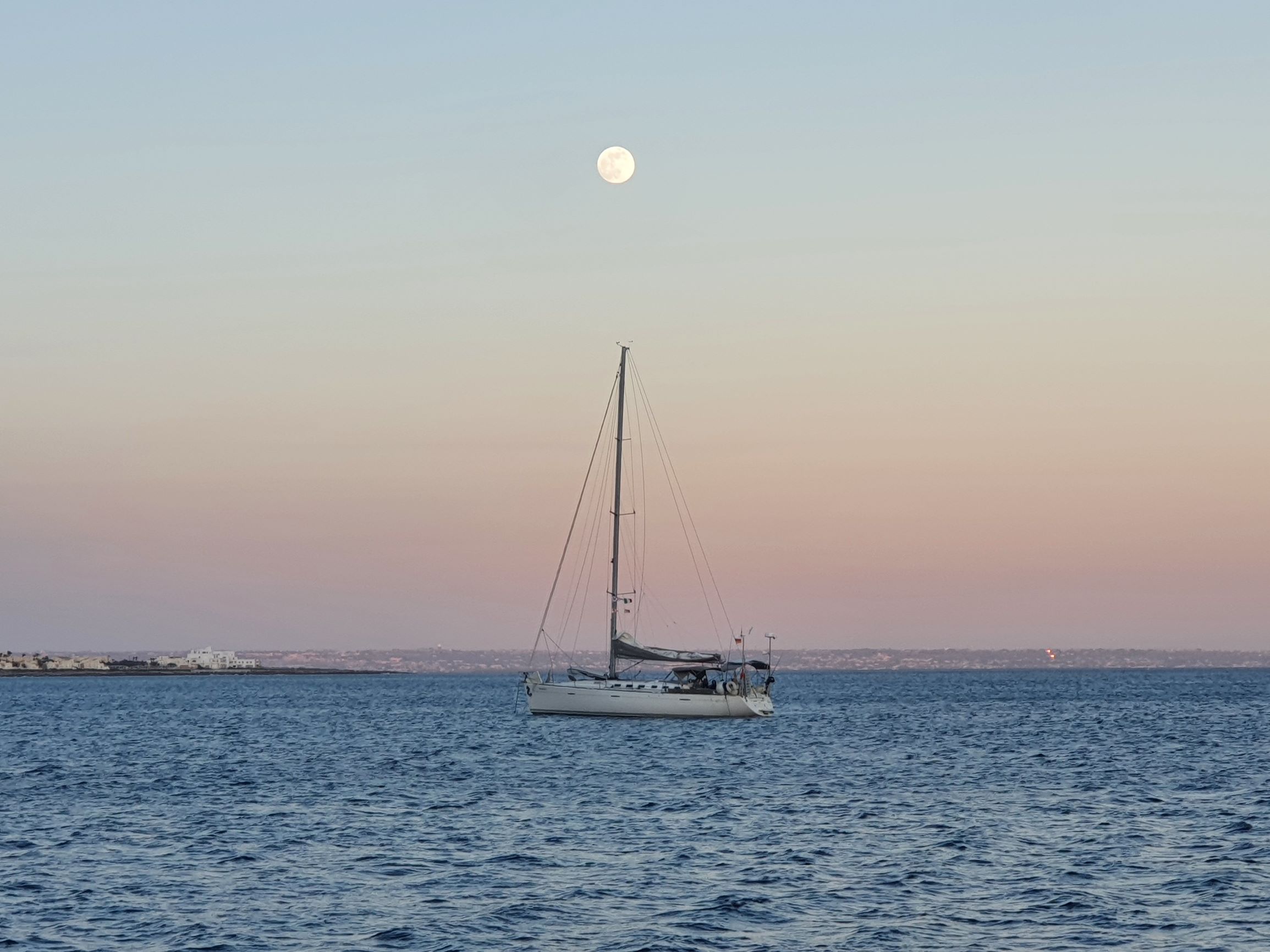 Segelschiff vor Anker in großer Bucht bei Sonnenuntergang und Vollmond.